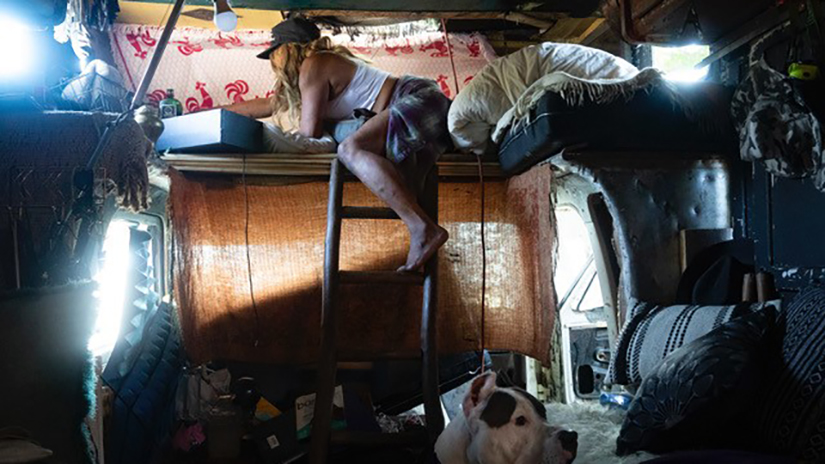 Rebecca Dannenbaum, a Venice Beach native known by her friends as Prophet, searching for a phone charger on her bed in the RV that she lives on Venice Blvd. in Los Angeles, Calif., on Sunday, Sept. 24, 2023. Dannenbaum was adopted by a Jewish family at three weeks old and moved to Venice when she was almost four. She has spent all but 14 years of her life AWOL, “Always West of Lincoln.” Photo by Caylo Seals.