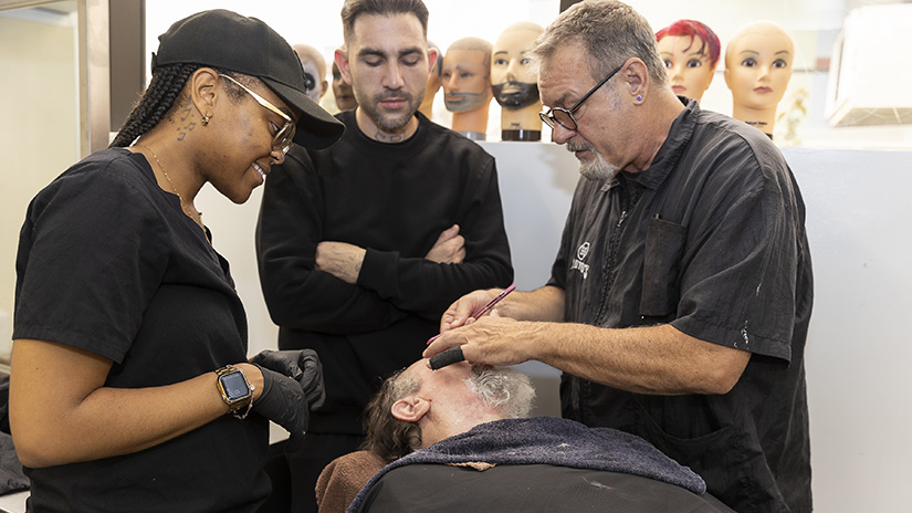 Barbering instructor Mr. Rick Harrison demonstrating beard shaping with straight razor technique on client Warren alongside students Joy and Chad.