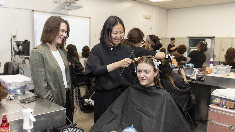 Debbie Perret supervising a student cutting a client's hair.